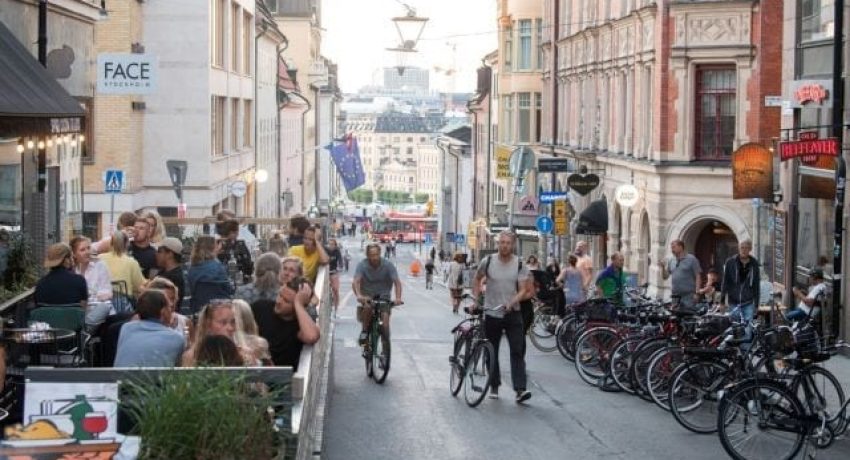People with bicycles pass by an outdoor restaurant on a street in the Sodermalm neighborhood