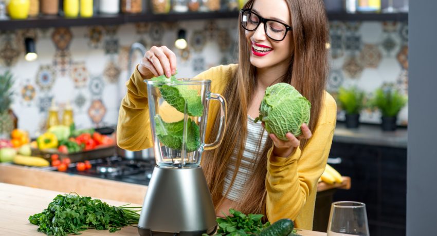 Young,Smiling,Woman,Making,Smoothie,With,Fresh,Greens,In,The