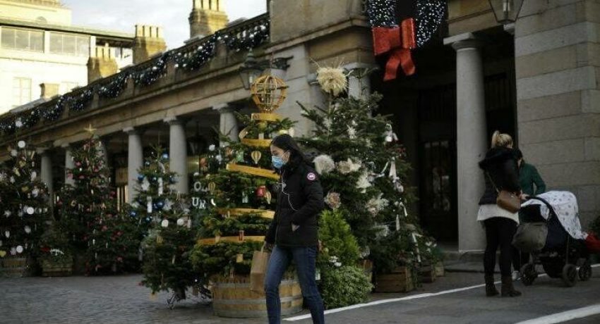 A woman wearing a face mask walks backdropped by Christmas trees in Covent Garden, during England's second coronavirus lockdown in London, Thursday, Nov. 26, 2020.  As Christmas approaches, most people in England will continue to face tight restrictions on socializing and business after a nationwide lockdown ends next week, the government announced Thursday. (AP Photo/Matt Dunham)