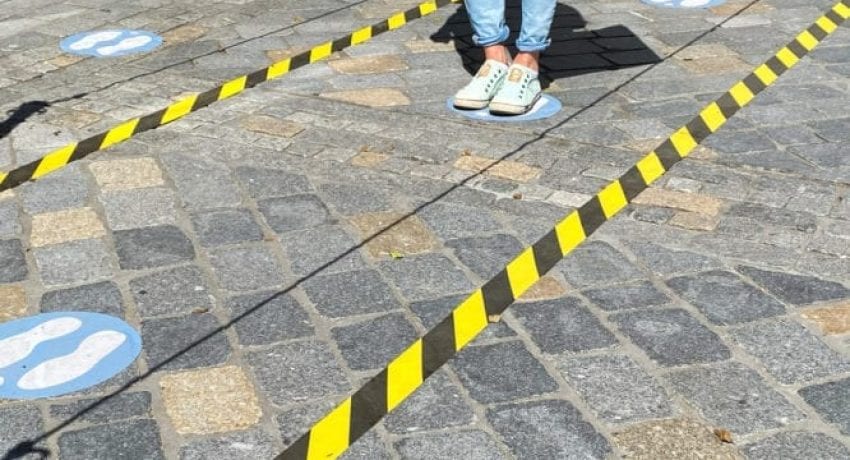 Roermond, Netherlands - May 19. 2020: View on feet of one person between do not cross tapes and blue markings to keep distance at shop entrance in corona crisis