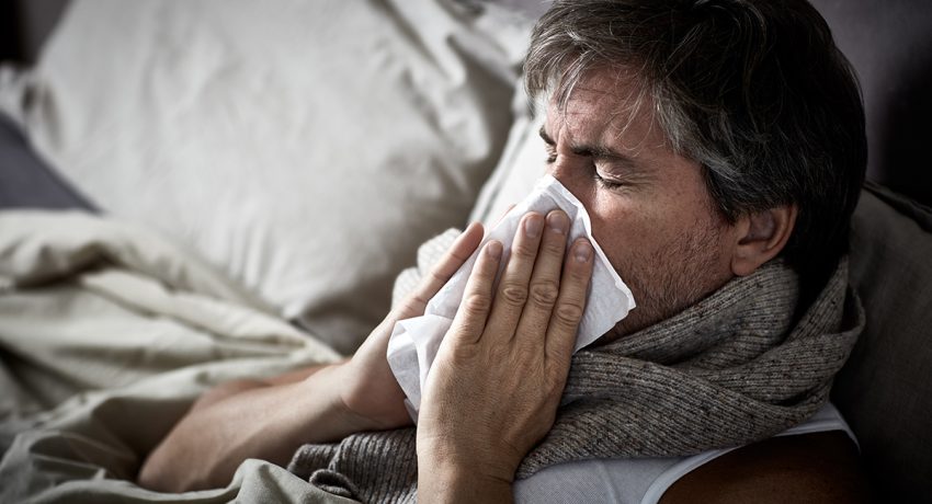 Sick man with flu lying in bed and blow nose napkin.