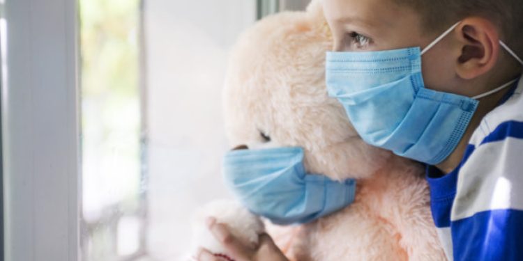 Sad child and his teddy bear both in protective medical masks looks out window. Virus protection, coronavirus pandemic. Coronavirus covid-2019.