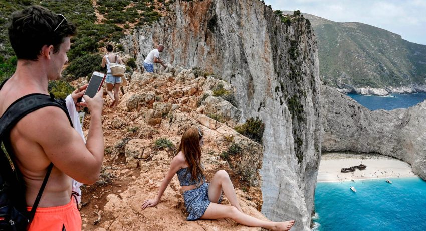 Tourists take pictures and selfies from a rock overlooking the famous Navagio (Shipwreck) beach on the Ionian island of Zakynthos on July 18, 2020. - Usually for the season, there is 20 daily departures for the island's landmark beach, now only four operate daily. (Photo by Louisa GOULIAMAKI / AFP) (Photo by LOUISA GOULIAMAKI/AFP via Getty Images)