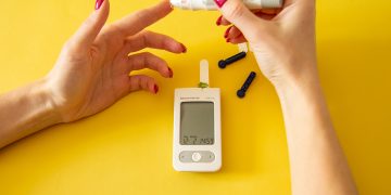 Diabet, great design for any purposes. Medical equipment. Medical concept. Close up of woman hands on yellow background using lancet on finger to check blood sugar level by Glucose meter